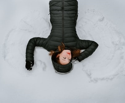 a women lays in the snow making a snow angel by fanning out her arms and legs to make wings in the snow