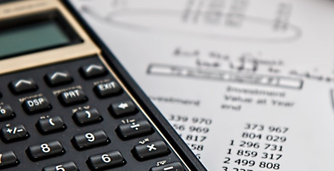 Calculator sitting on top of paper with money calculations