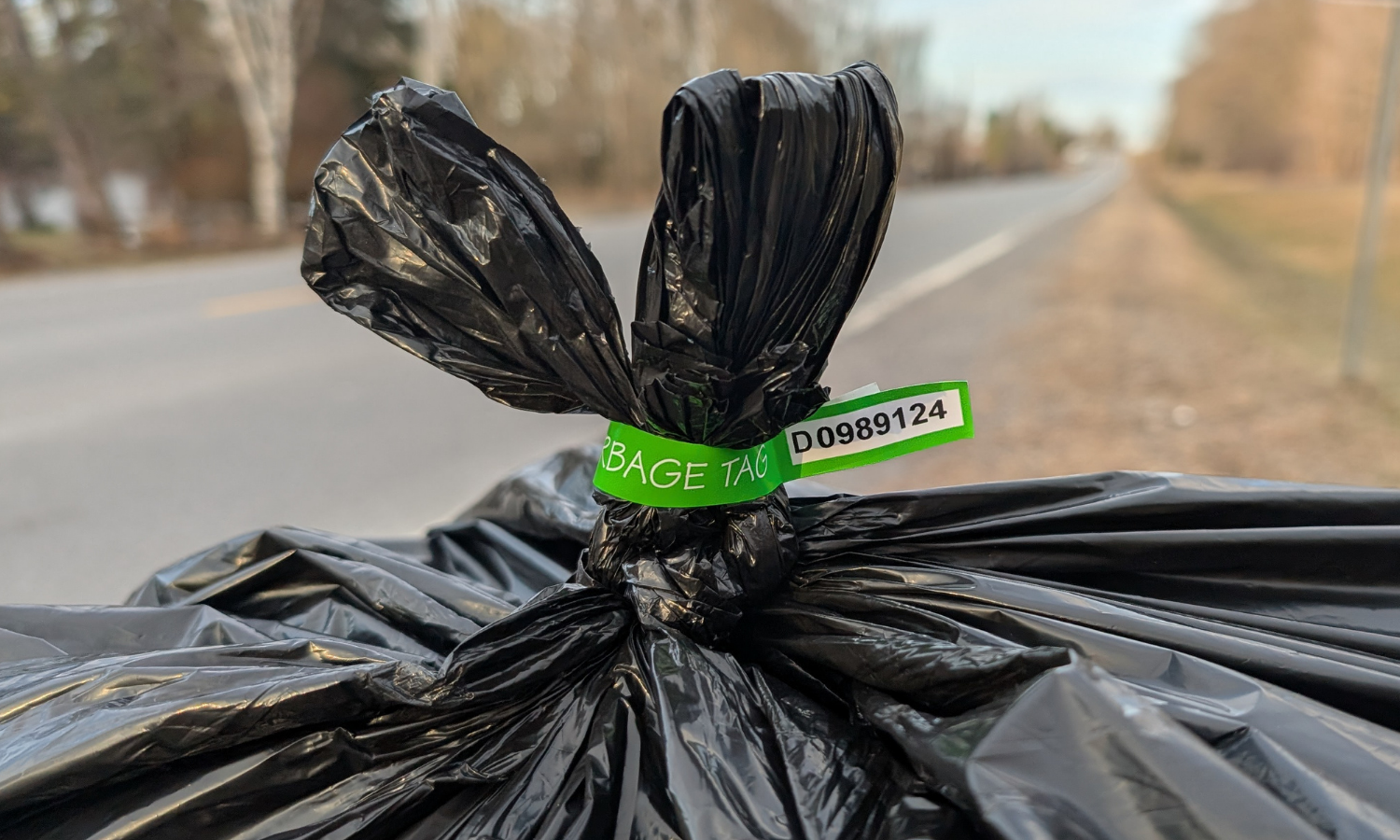 Photo of a garbage bag with a green bag tag attached to the top.
