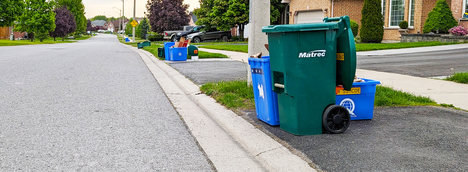 Recycling blue bins and a organics green bin at the curb for collection.