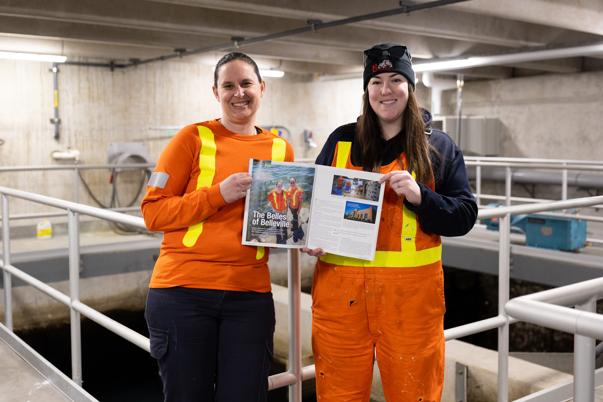 Photo of Amy and Joanne holding the magazine they are featured in, with the water treatment plant in the background.