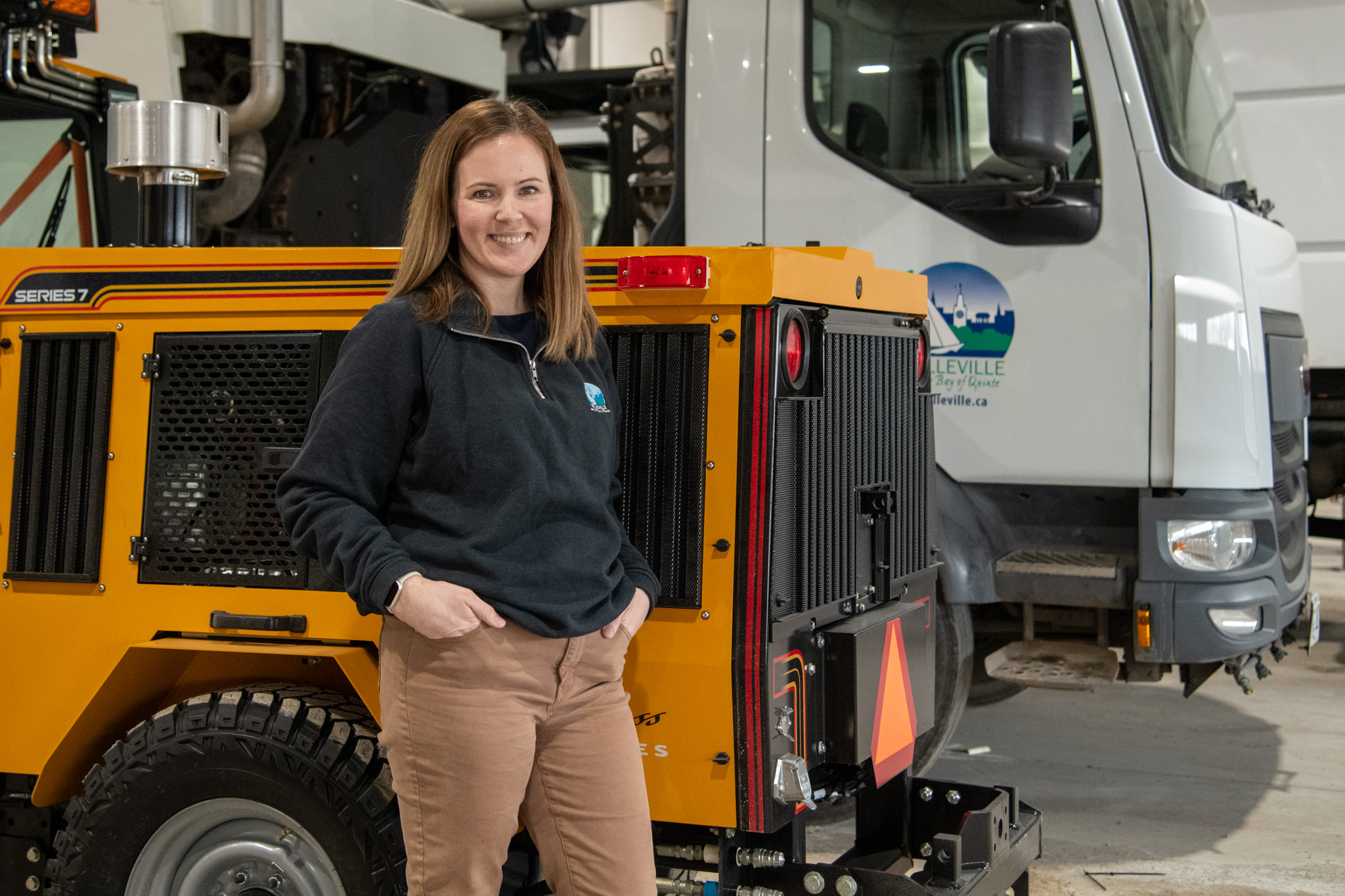Photo of Deanna beside a sidewalk plow and street sweeper.