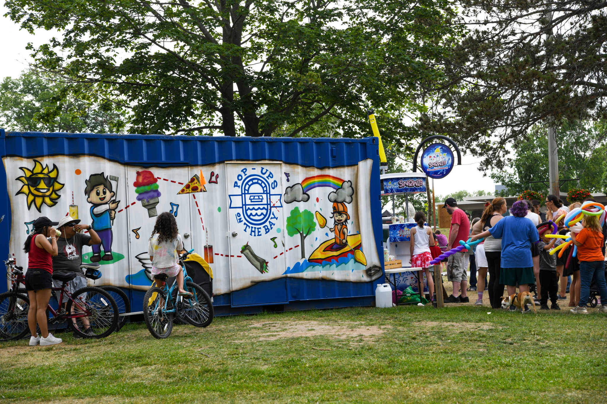 A photo of a Pop-ups on the bay vendor with a mural on the side of the building with the Pop-ups on the Bay Logo with a family on bicycles in front of it.