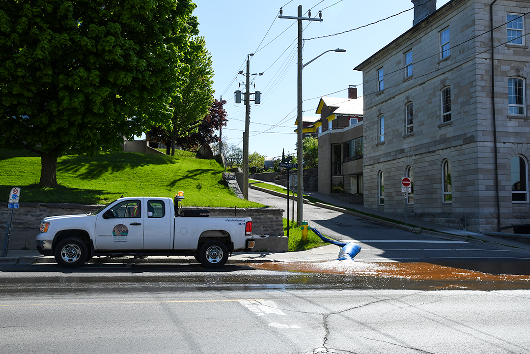 City vehicle parked on side of road as a large blue tube washes reddish-coloured water into the street