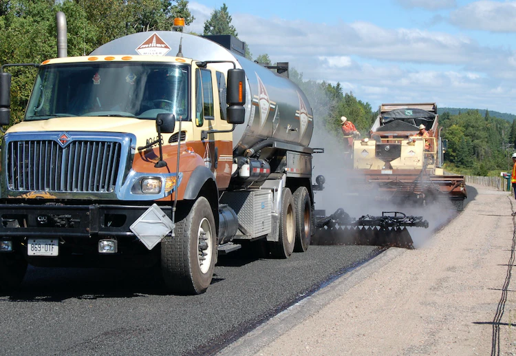 Photo of a dump truck applying a slurry seal to a road.
