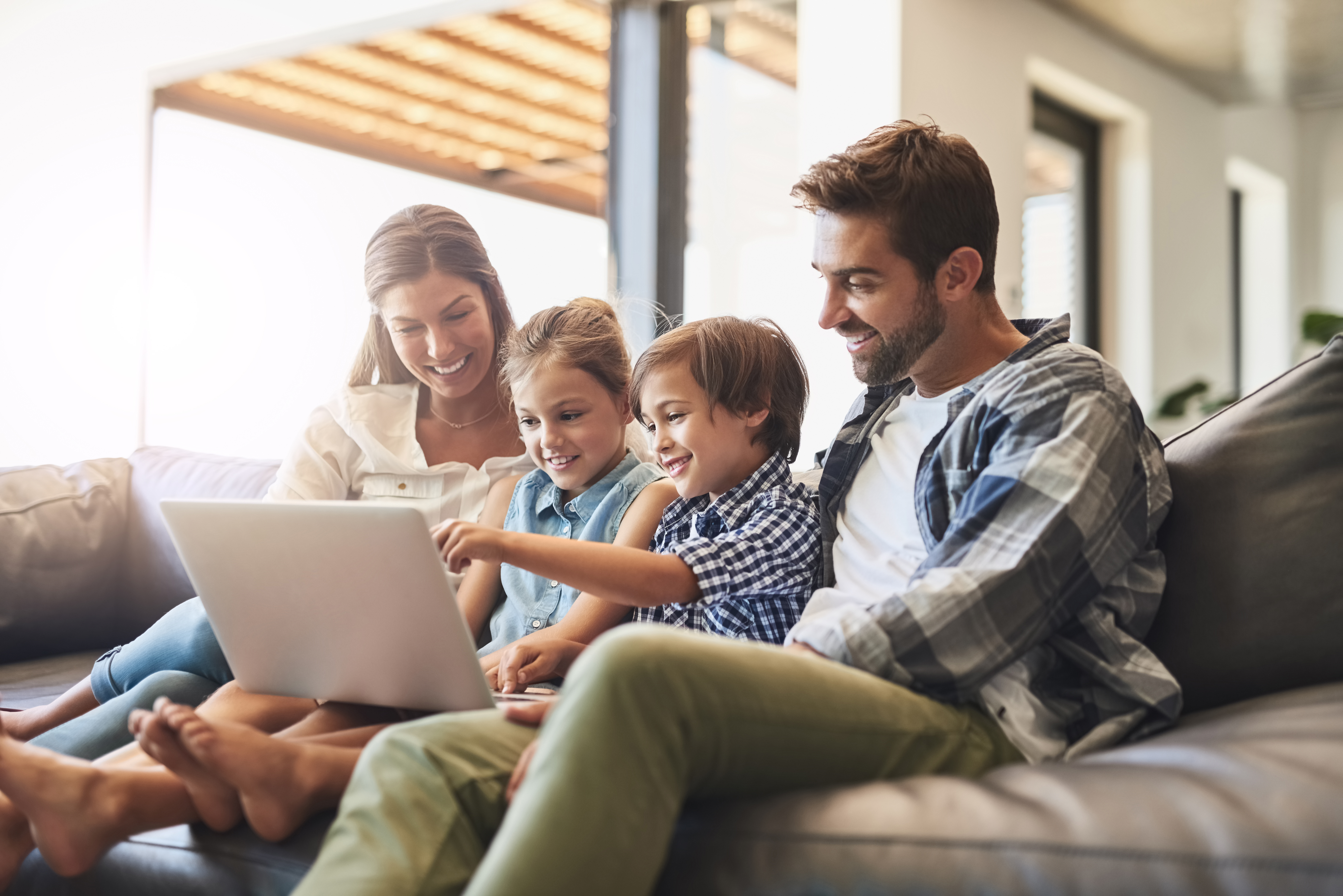 Shot of a mother and father using a laptop with their son and daughter on the sofa at home.